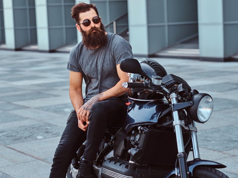 brutal-bearded-male-in-a-gray-t-shirt-and-black-pants-sitting-on-his-custom-made-retro-motorcycle.jpg