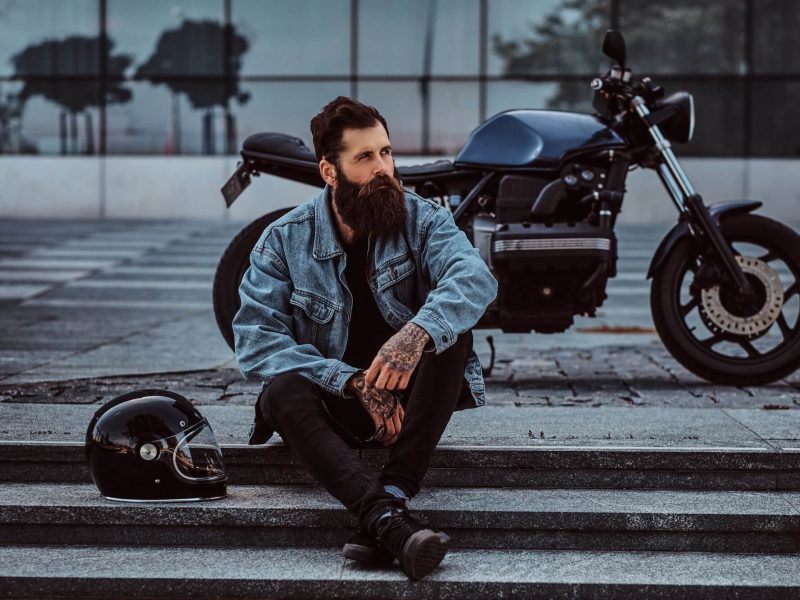 brutal-bearded-male-sitting-on-steps-near-his-custom-made-retro-motorcycle-against-skyscraper-1-1.jpg